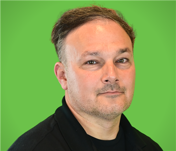 A male SERVPRO employee smiles infront of a green background.